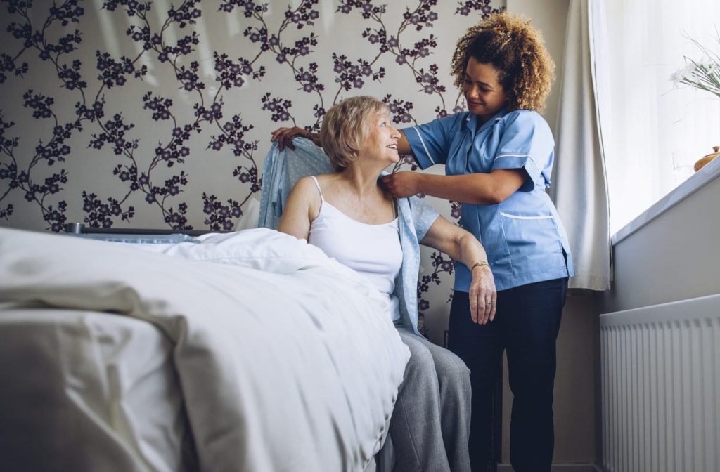 senior getting help from nurse to get her shirt back on. 