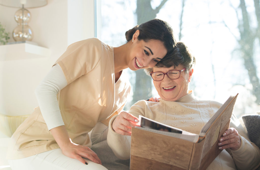 Happy senior women with younger woman going over book together on sofa