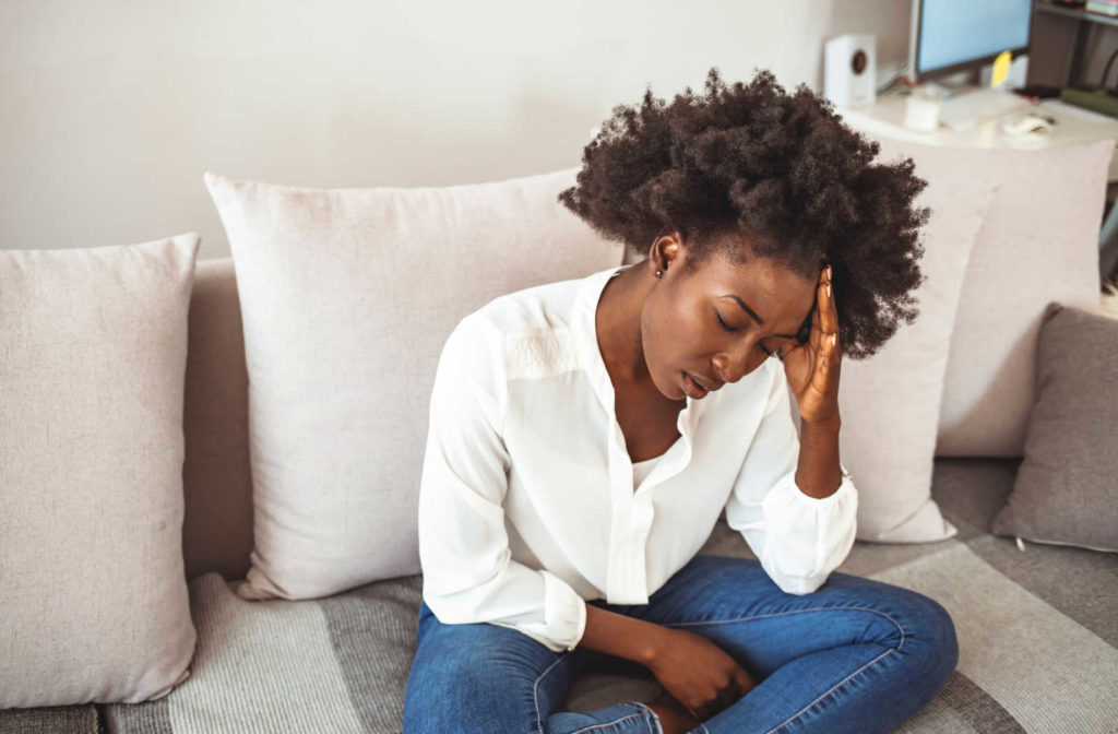 A young worn out woman sitting on the couch while holding her head.