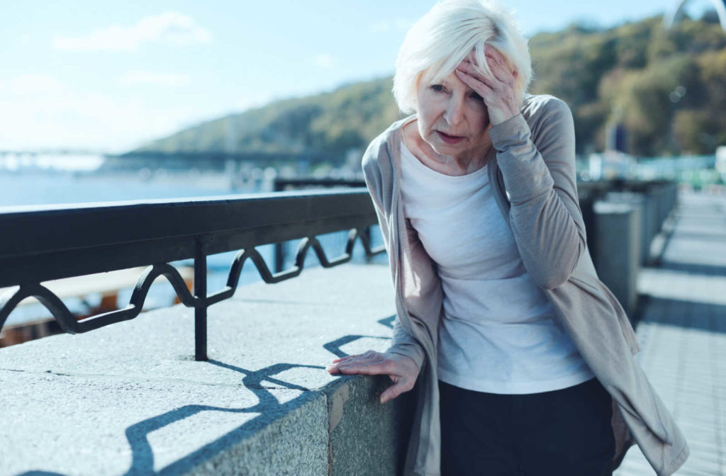An older lady leaning on a barrier and touching her forehead, losing her balance due vision problem.