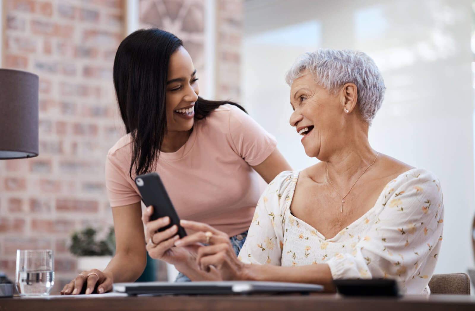 A senior woman holding a smartphone and talking to her daughter in a living room.