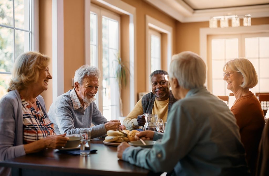 A group of seniors sitting around a table laughing while eating lunch in a senior living community.