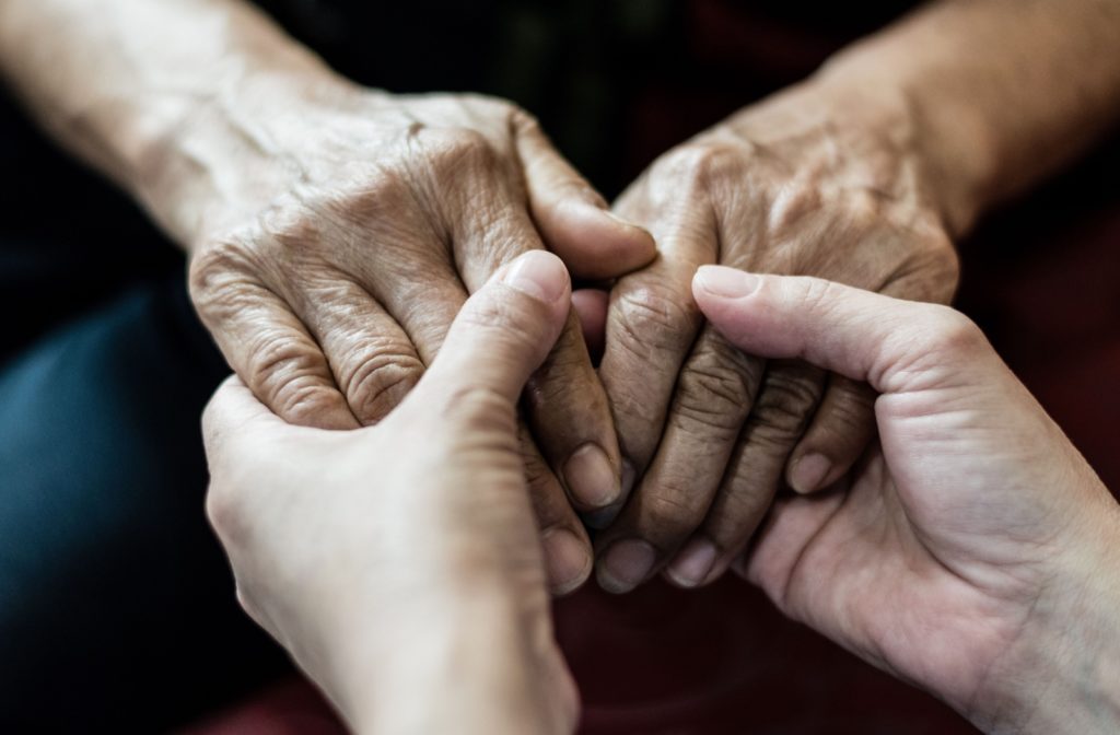 A pair of older adult hands held by younger adult hands.