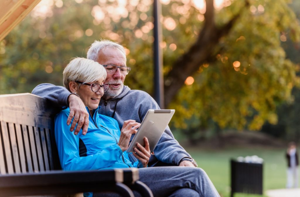 Senior couple outdoors on a park bench smiling and looking at a tablet together emphasizing the importance of secure online activity