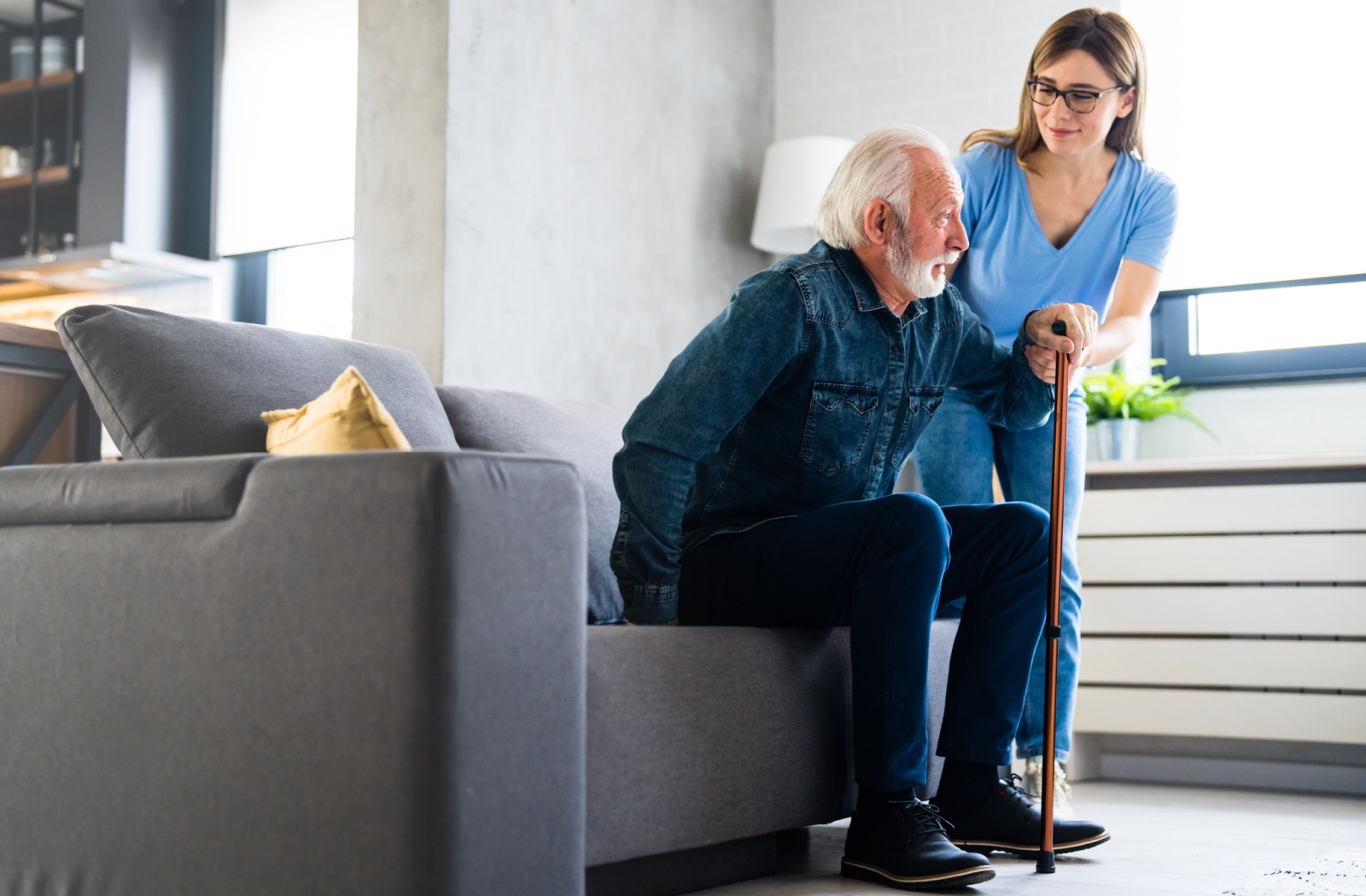 A nurse assisting an elderly man with a cane to stand up in an assisted living community.