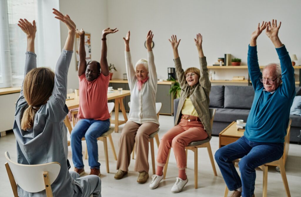 A group of assisted living residents participating in a modified exercise class while sitting on chairs.