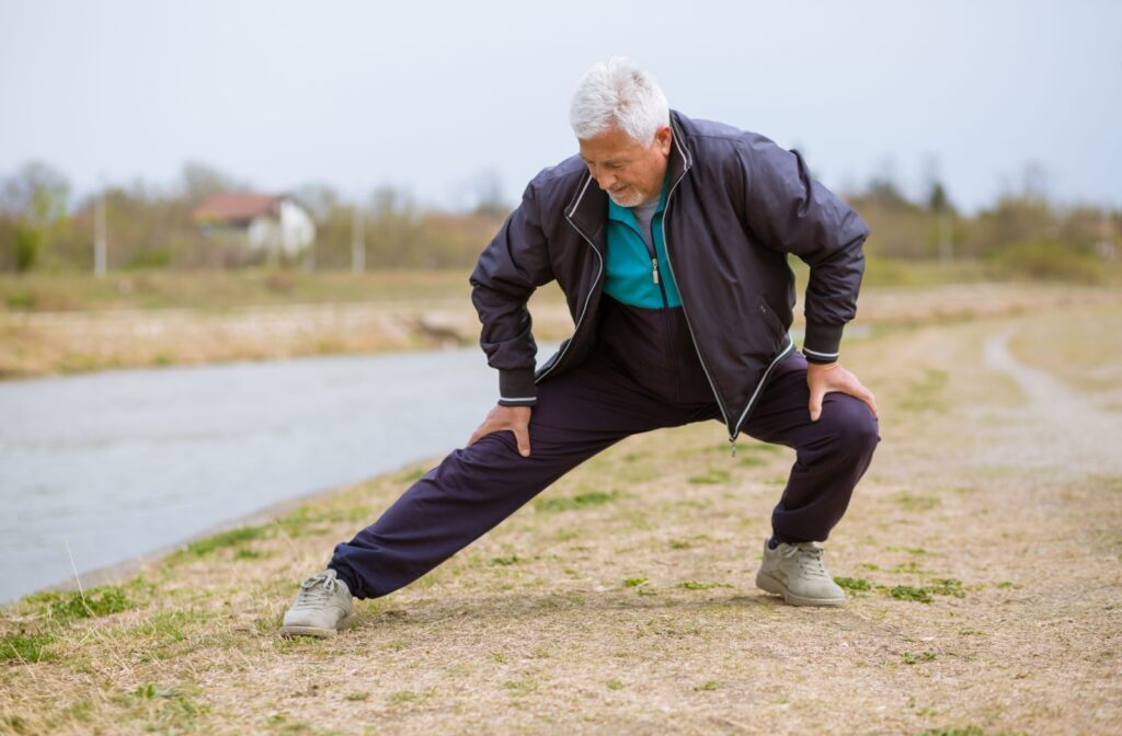 A senior man dressed in athletic clothing performing a side lunge stretch before going for a walk.