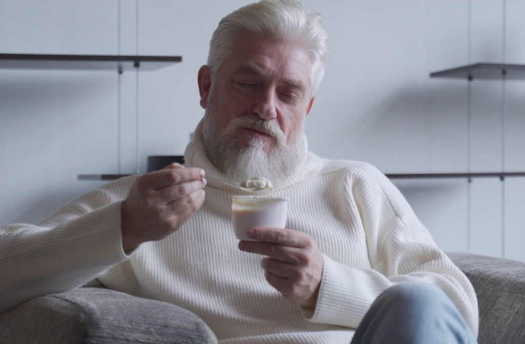 A senior in a white sweater snacks on a cup of yogurt and granola as a healthy snack option