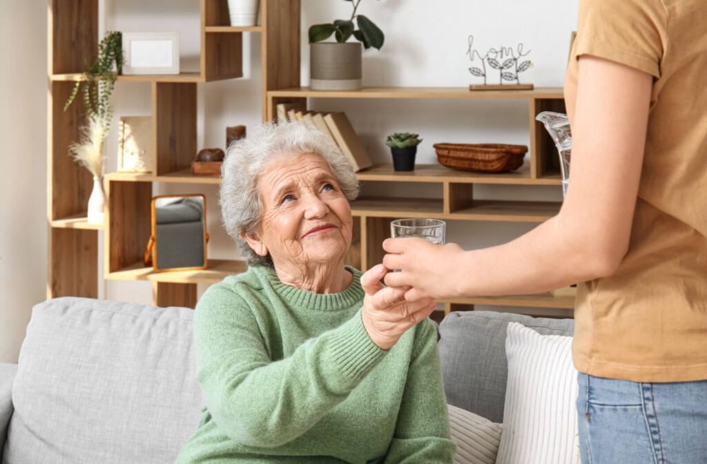 A senior in a green sweater accepts a glass of water from a family member helping them stay hydrated