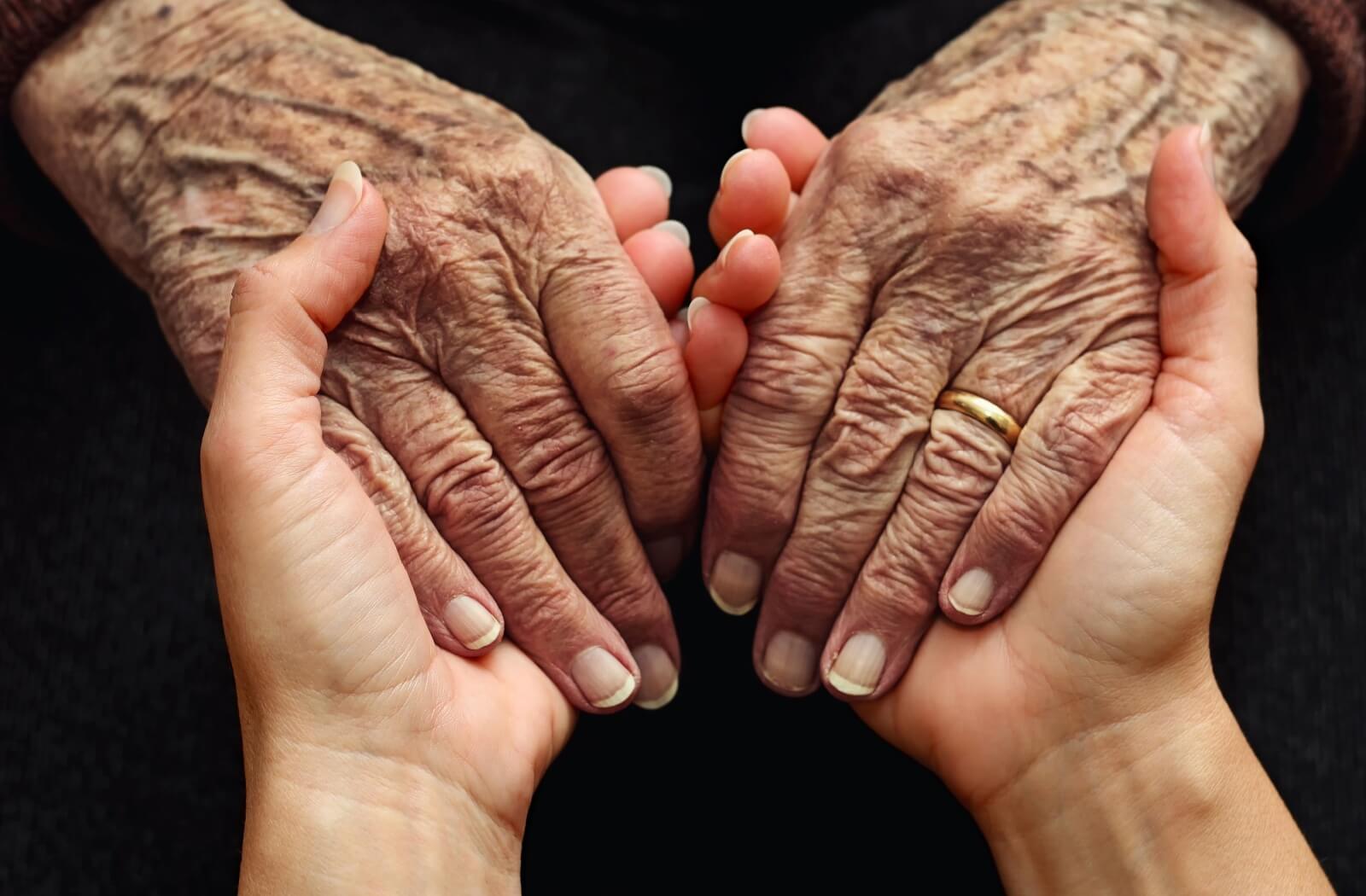 Someone holds an older adult's hands in a caring and compassionate way.