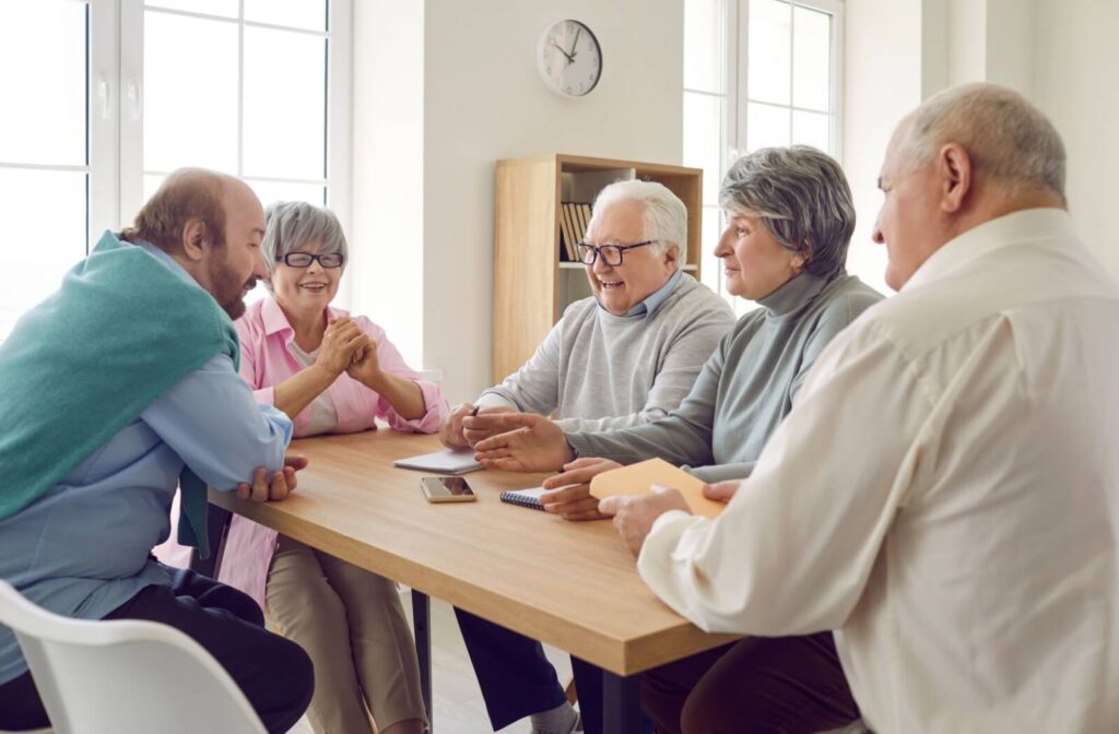 A group of older adults sit around a table socializing while in respite care.