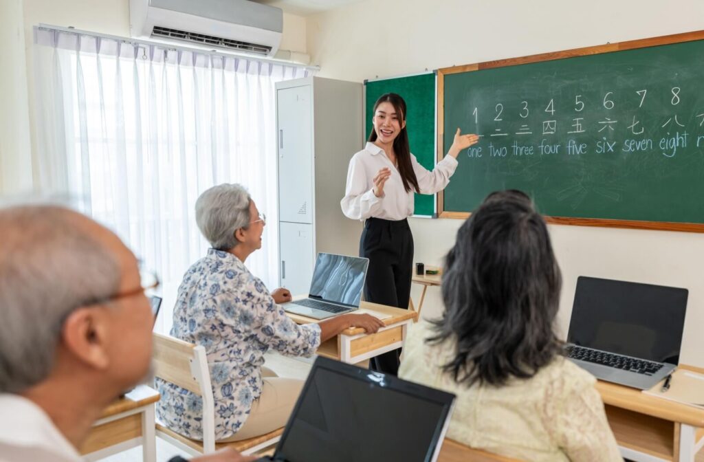 A teacher uses a chalkboard in a classroom to help seniors with learning the basic numbers in a new language